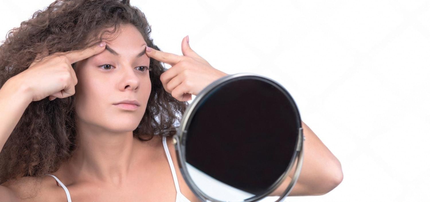 Woman checking her skin in the mirror as part of a home skincare routine